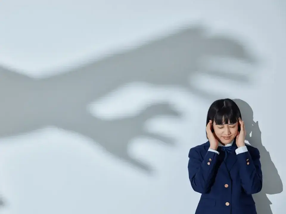 Frau hält sich die Ohren zu, hinter ihr der Schatten einer Hand